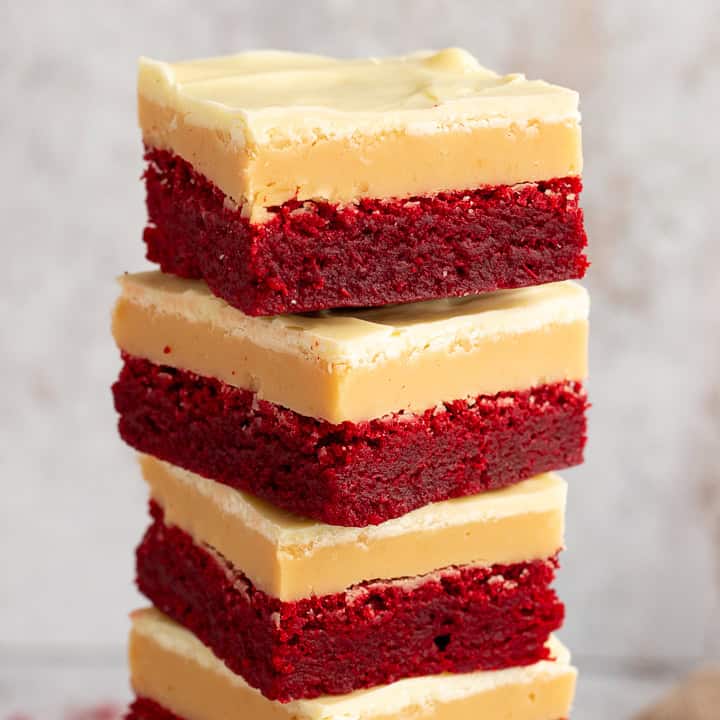 A close up of 4 red velvet millionaire brownies in a stack set against a mottled light background.