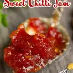 A close up of sweet chilli jam on a gold spoon set on a grey wooden backdrop with lettuce and chilli flakes in the background.
