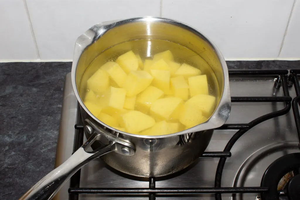 Chopped potatoes in a pan of cold salted water on the hob
