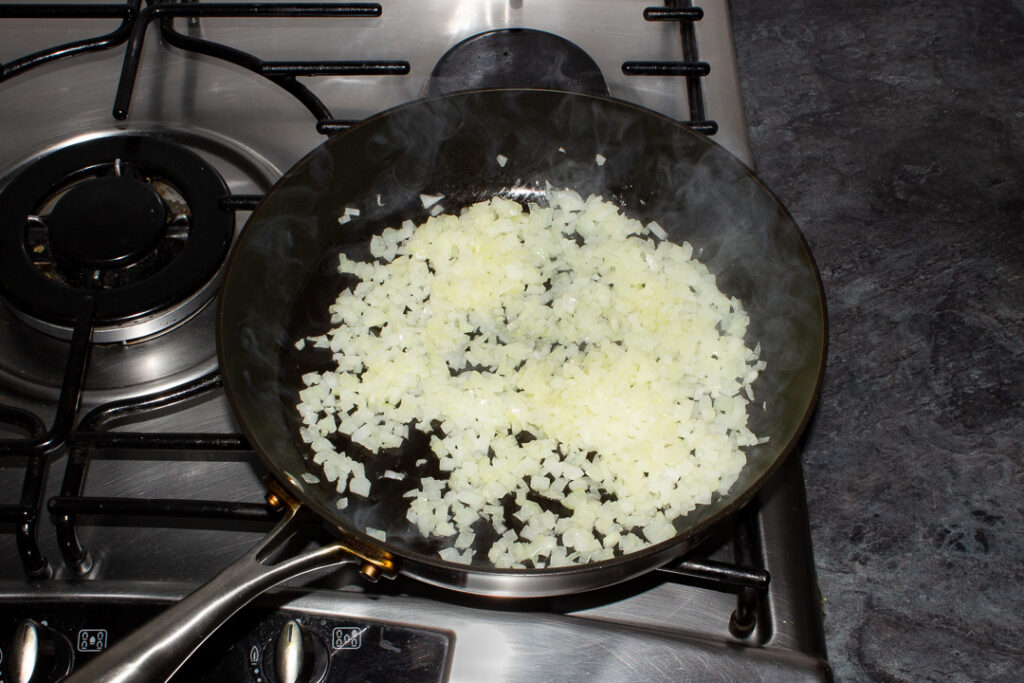 Diced onion frying in olive oil in a frying pan on the hob