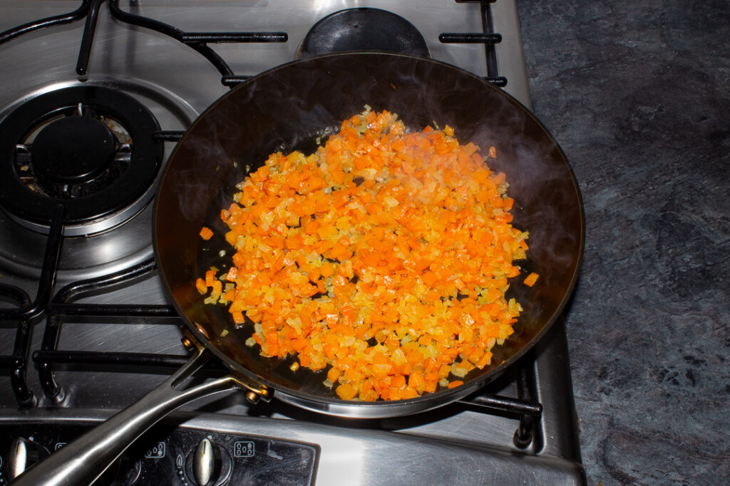 Diced onion and carrot cooking in oil in a frying pan on the hob