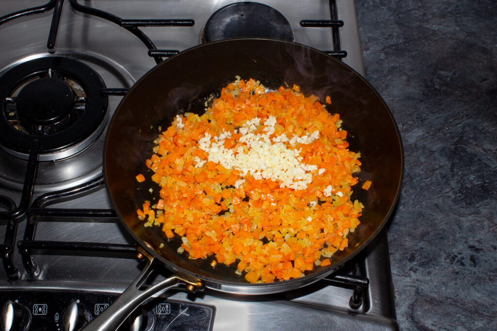 Diced onion, carrot and minced garlic cooking in oil in a frying pan on the hob