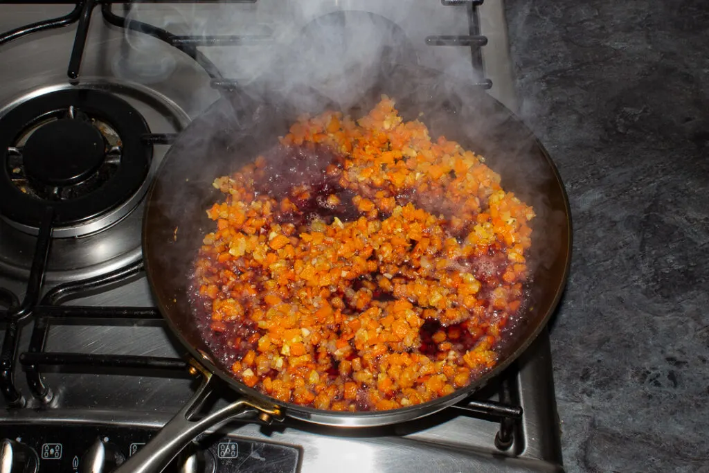 Onion, carrot, garlic, flour and red wine cooking in a frying pan on the hob