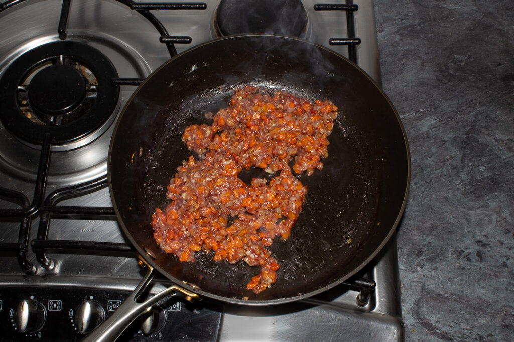 Sticky onion, carrot, garlic, flour and red wine cooking in a frying pan on the hob