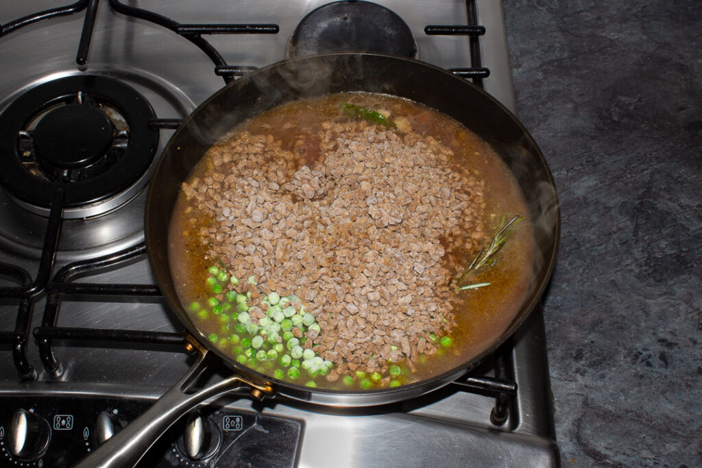 Vegetarian shepherd's pie sauce base, herbs, frozen peas and soya mince cooking in a frying pan on the hob