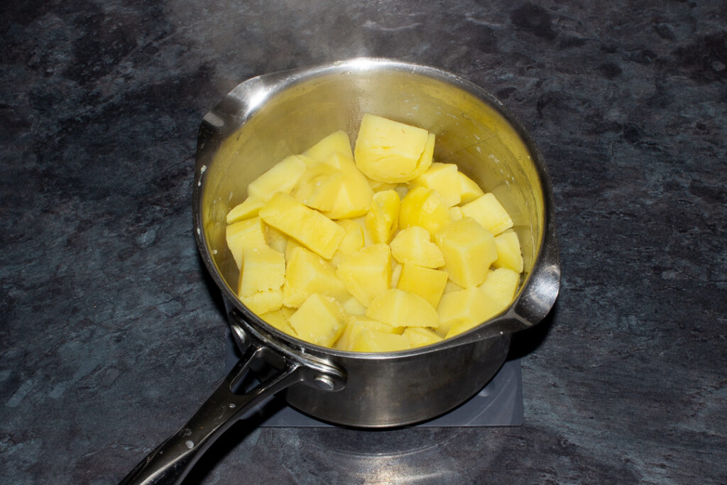 Boiled and drained chopped potatoes in a large saucepan on a kitchen worktop