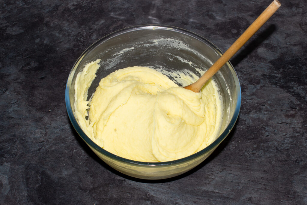 Creamy mashed potato and melted butter in a glass bowl with a wooden spoon on a kitchen worktop