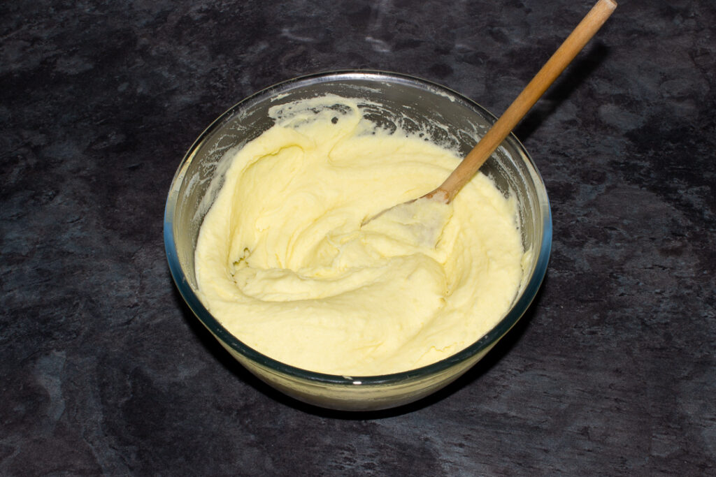 Creamy mashed potato, melted butter and milk in a glass bowl with a wooden spoon on a kitchen worktop