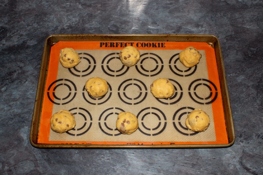 Creme Egg cookie dough balls spaced apart on a lined baking tray