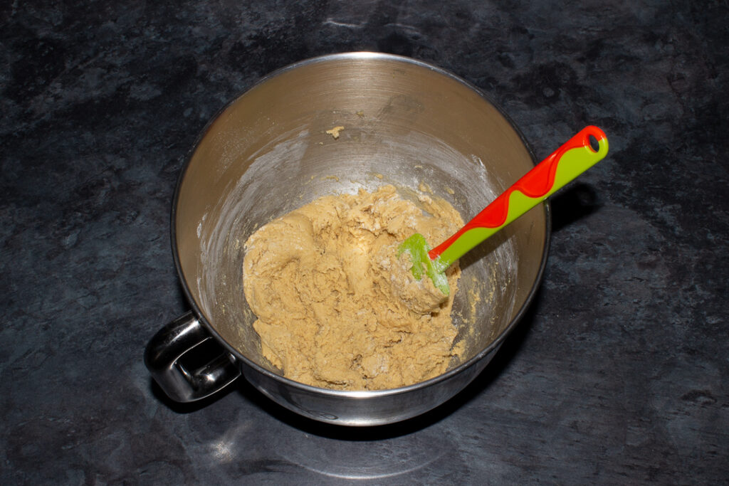 Cookie dough in the bowl of an electric stand mixer with a green spatula