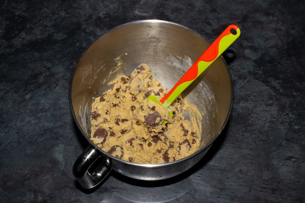 Creme Egg cookie dough in the bowl of an electric stand mixer with a green spatula