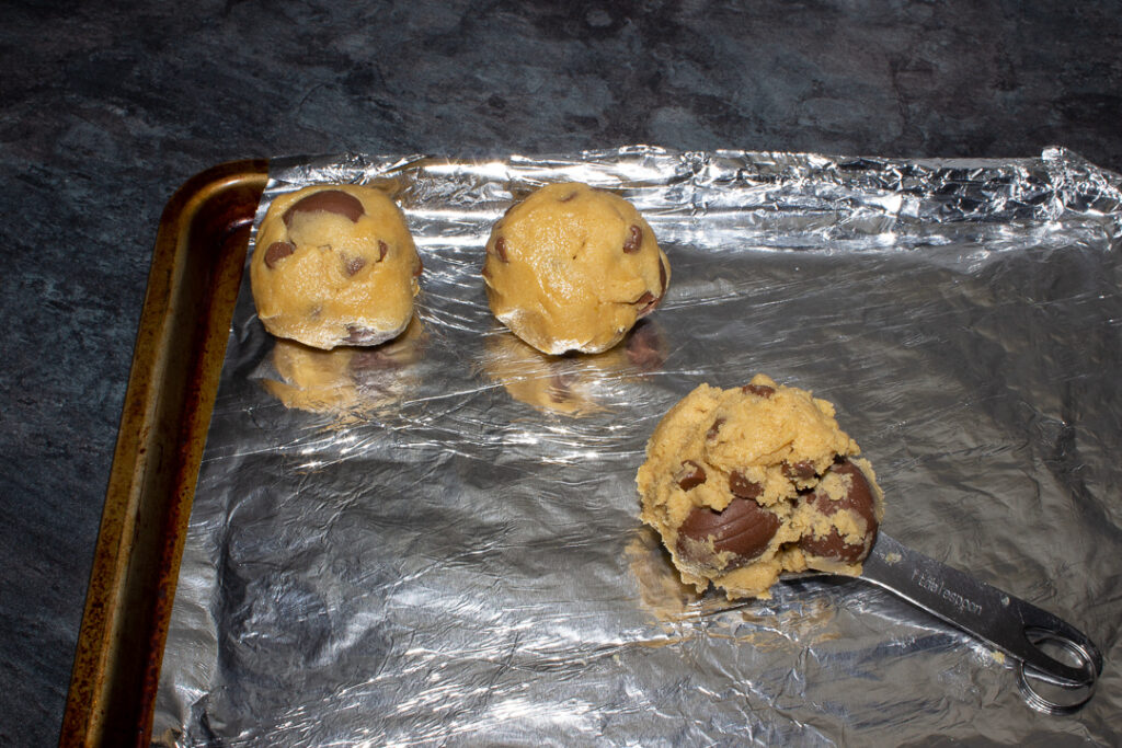 Creme Egg cookie dough being rolled into balls and put on a foil lined tray