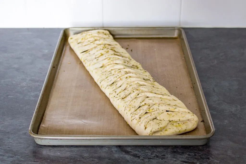 An unbaked stromboli on a lined baking tray. Brushed with olive oil and dried herbs