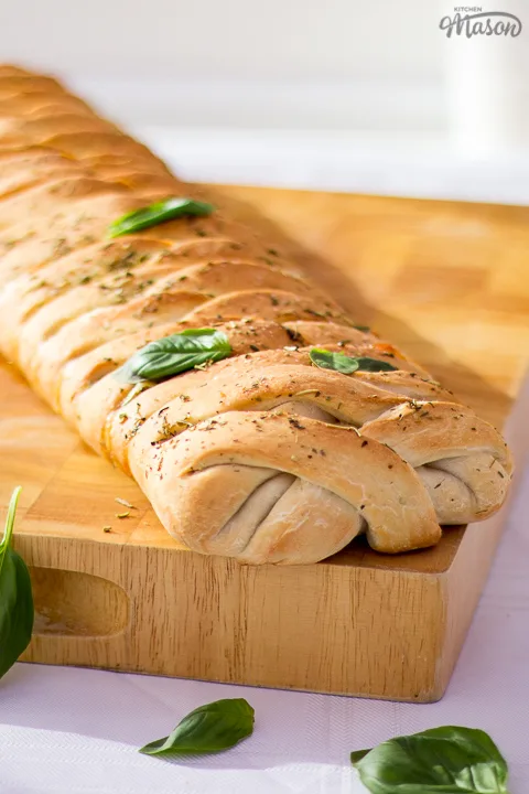 Baked stromboli on a wooden chopping board scattered with fresh basil leaves