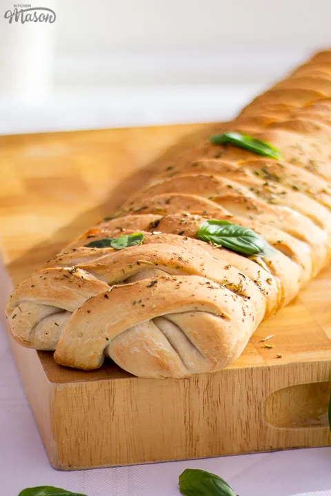 Baked stromboli on a wooden chopping board scattered with fresh basil leaves