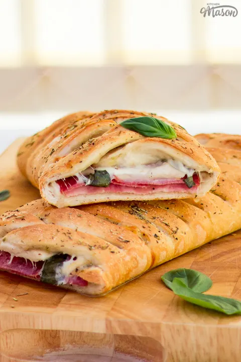 Baked stromboli cut in half on a wooden chopping board scattered with fresh basil leaves