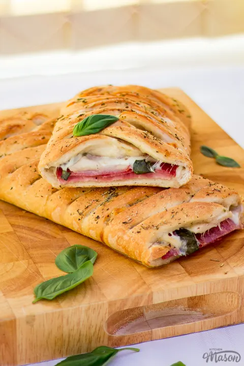 Baked stromboli cut in half on a wooden chopping board scattered with fresh basil leaves