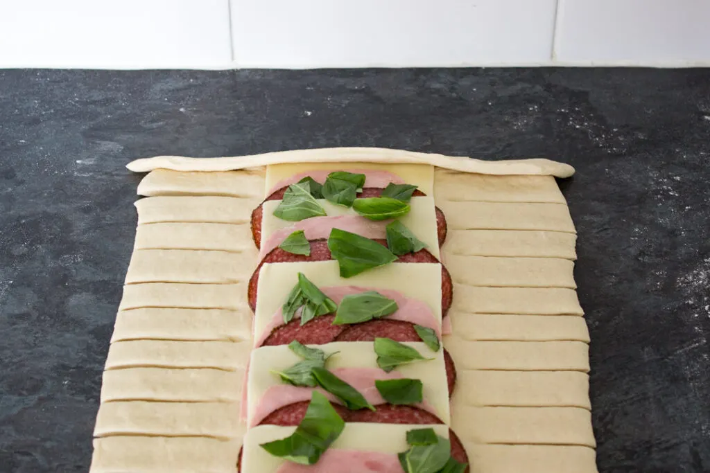 Pizza dough and fillings being folded into a latticed stromboli