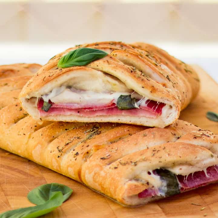 Baked stromboli cut in half on a wooden chopping board scattered with fresh basil leaves