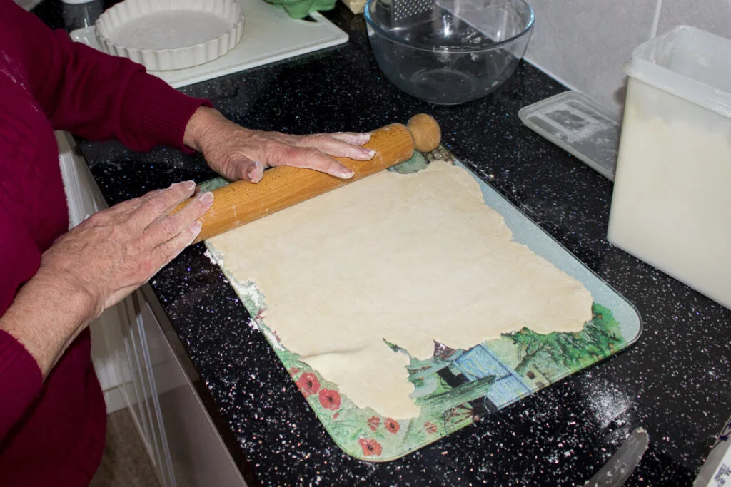 Gran rolling out the pastry with a rolling pin on a kitchen worktop
