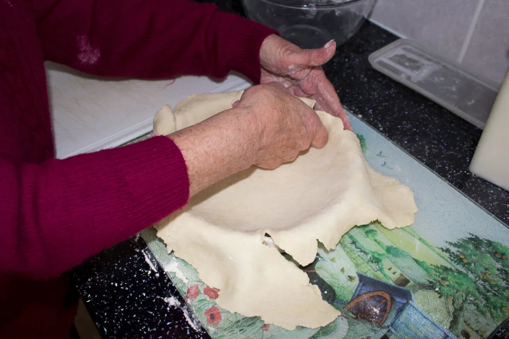 Gran pressing the pastry into the baking dish on a kitchen worktop
