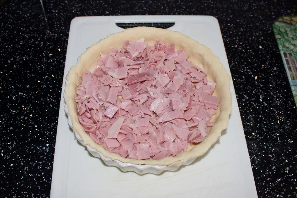 Lots of chopped ham in a baking dish lined with an unbaked pastry case