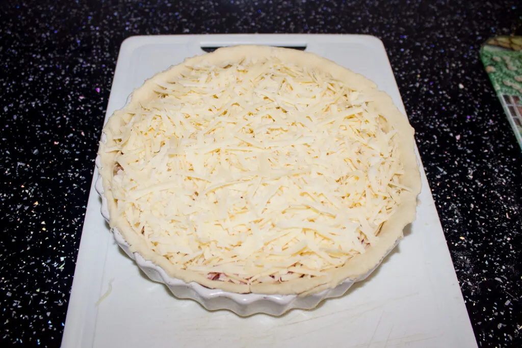 Lots of chopped ham and grated cheese in a baking dish lined with an unbaked pastry case