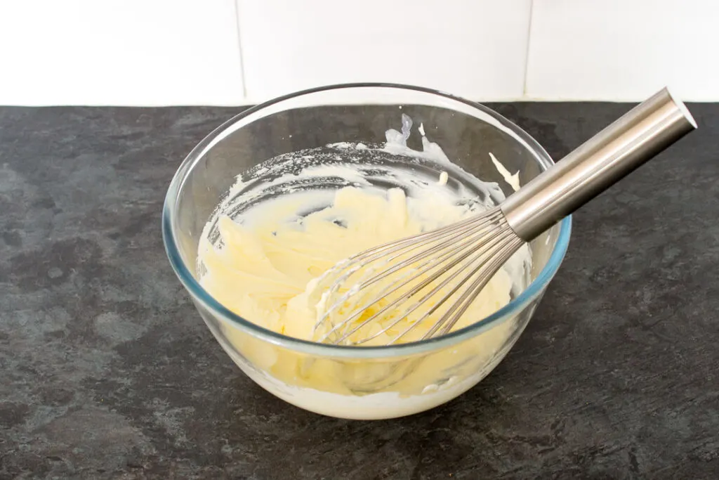 Cream whipped to stiff peaks in a glass bowl with a hand whisk