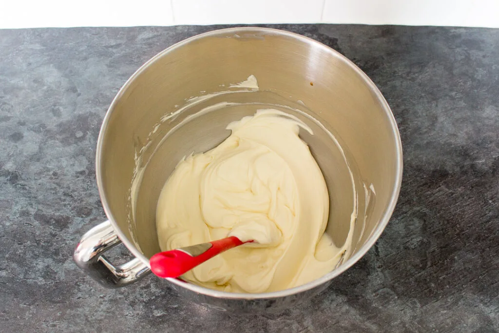 Cream cheese, sugar, vanilla and whipped double cream folded together in a bowl with a spatula