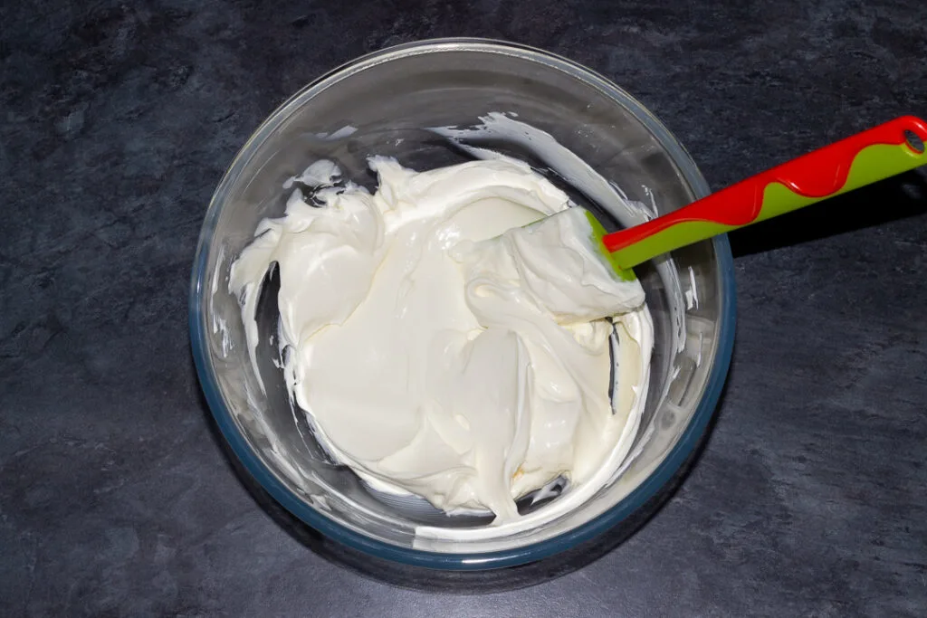 Cream cheese beaten until softened with a spatula in a glass bowl on a kitchen worktop.
