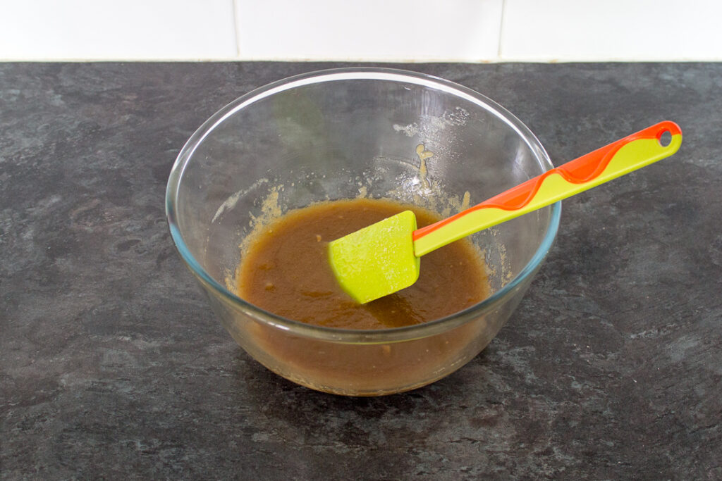 Melted butter and sugar mixed together in a glass bowl with a spatula.