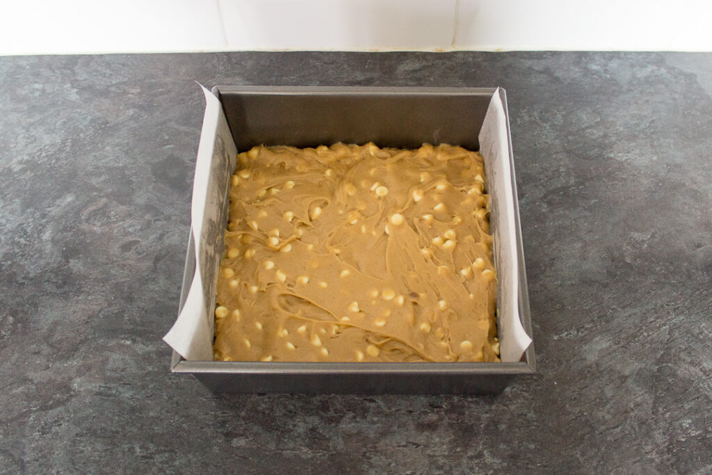 White chocolate blondie batter pressed into a lined square baking tin.