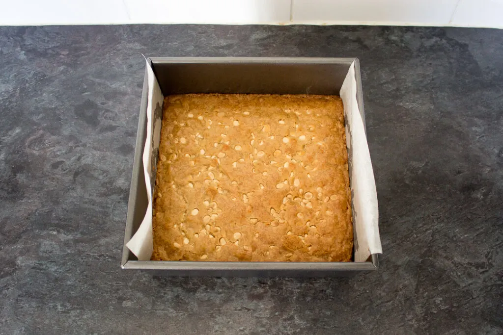 Baked white chocolate blondie in a lined square baking tin.