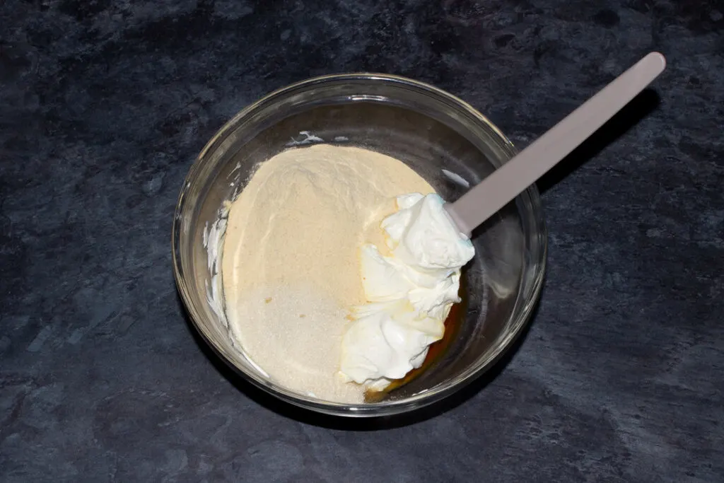 Softened cream cheese in a mixing bowl with sugar, malt powder and a spatula.