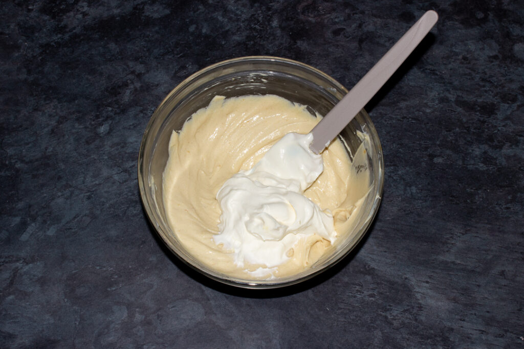 Malteser cheesecake filling having whipped cream folded into it in a mixing bowl with a spatula.