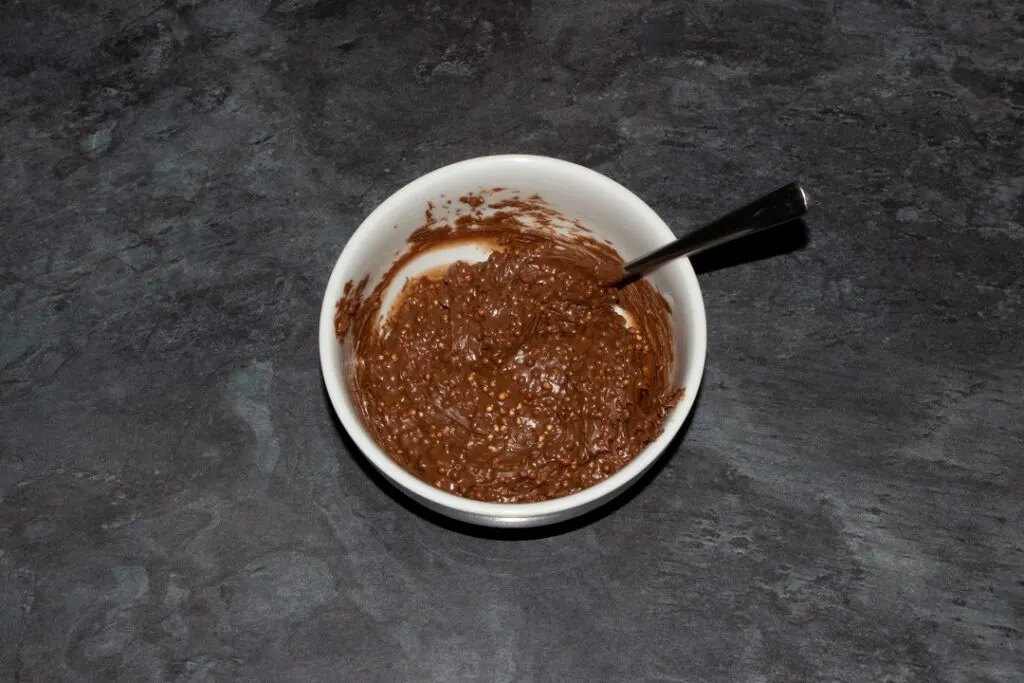 Softened Maltesers spread in a small bowl with a spoon on a kitchen worktop.