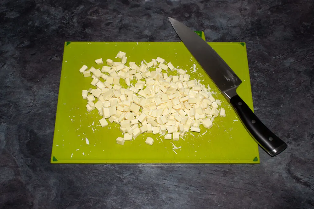 White chocolate that's been chopped into chunks on a green chopping board with a sharp knife