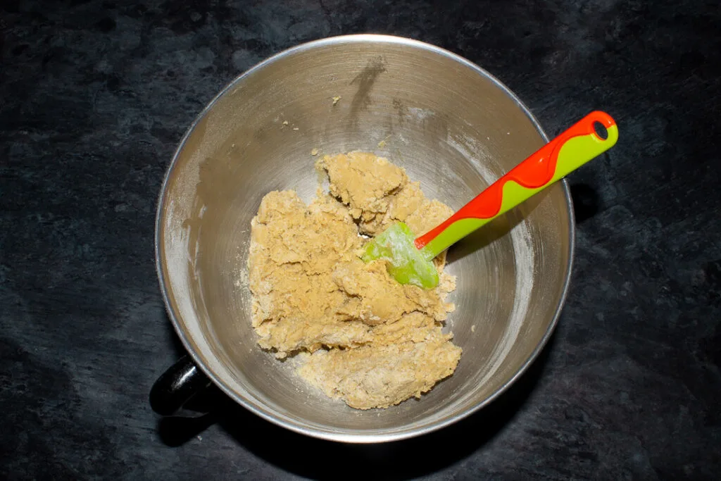 Cookie dough in an electric stand mixer with a green spatula