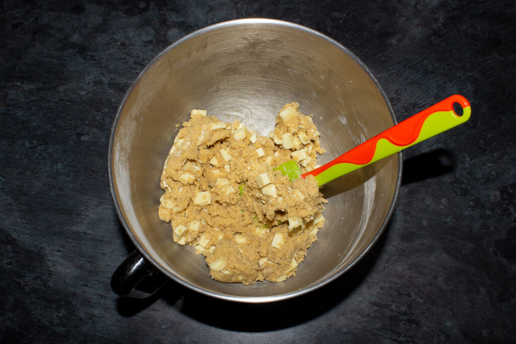 White chocolate cookie dough in the bowl of an electric stand mixer with a green spatula