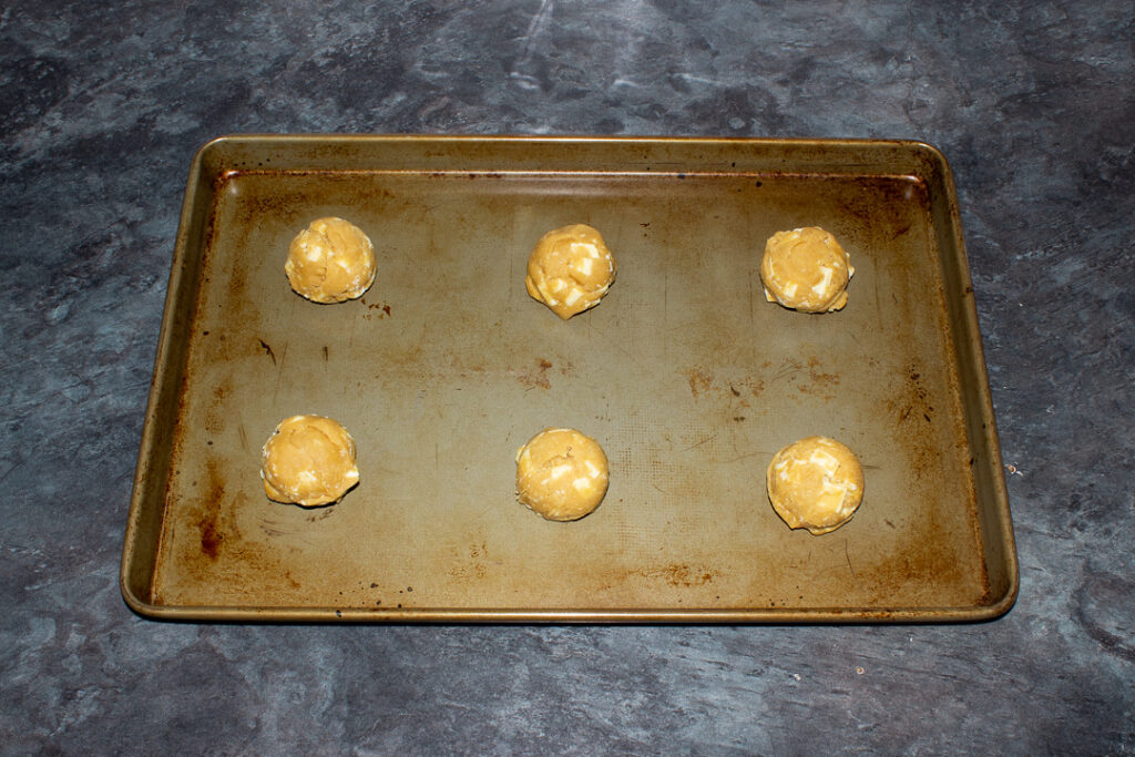6 white chocolate chip cookie dough balls spaced out on a large baking tray