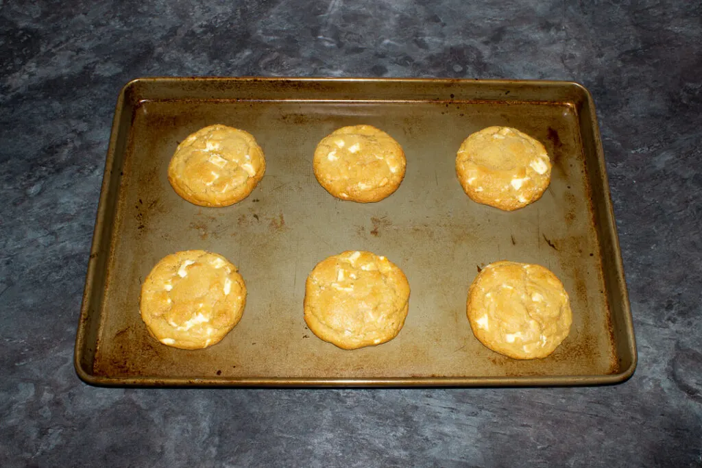 6 baked white chocolate chip cookies spaced out on a large baking tray