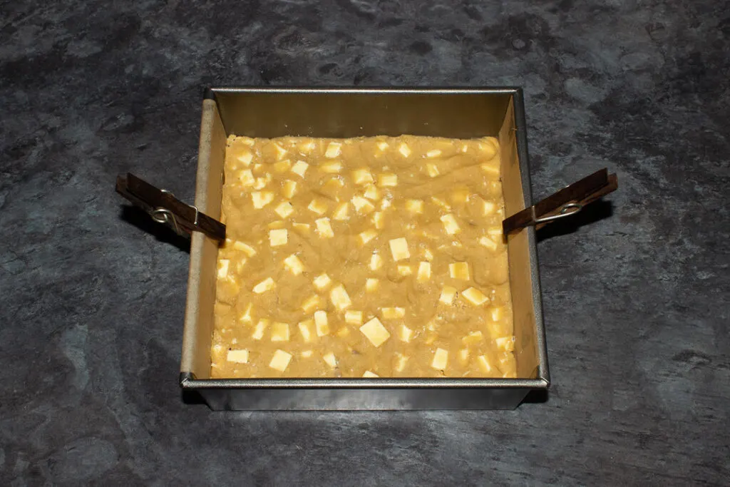 A lined square baking tin filled with 2 layers of white chocolate cookie dough and Kinder bars.