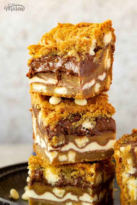 A stack of 3 white chocolate kinder nutella cookie bars on an iron plate. Set on a light cream backdrop.