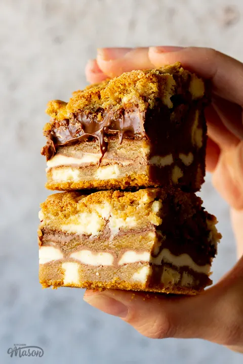 2 white chocolate kinder nutella cookie bars being held in a stack by a hand against a cream backdrop