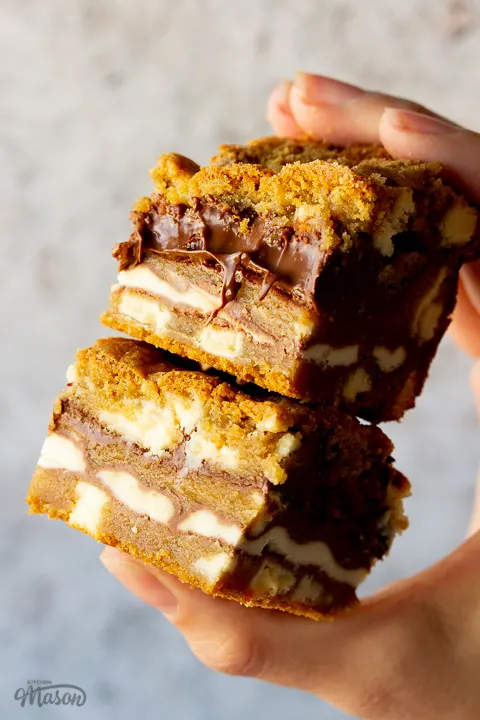 2 white chocolate kinder nutella cookie bars being held in a stack by a hand against a cream backdrop