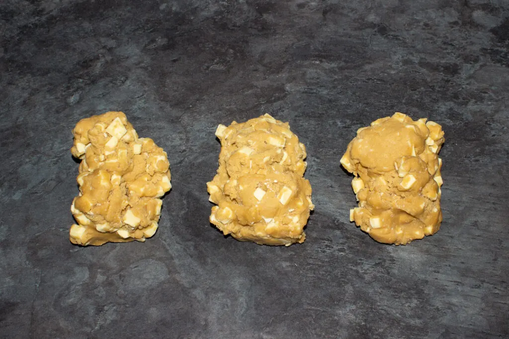 White chocolate chip cookie dough divided into 3 pieces on a kitchen worktop