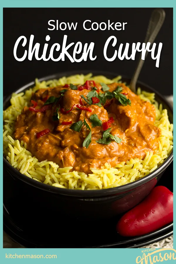 A black bowl filled with chicken curry over rice, topped with coriander and red chilli with a fork inside. Set on a black plate over a cream napkin with a whole red chilli in the background..
