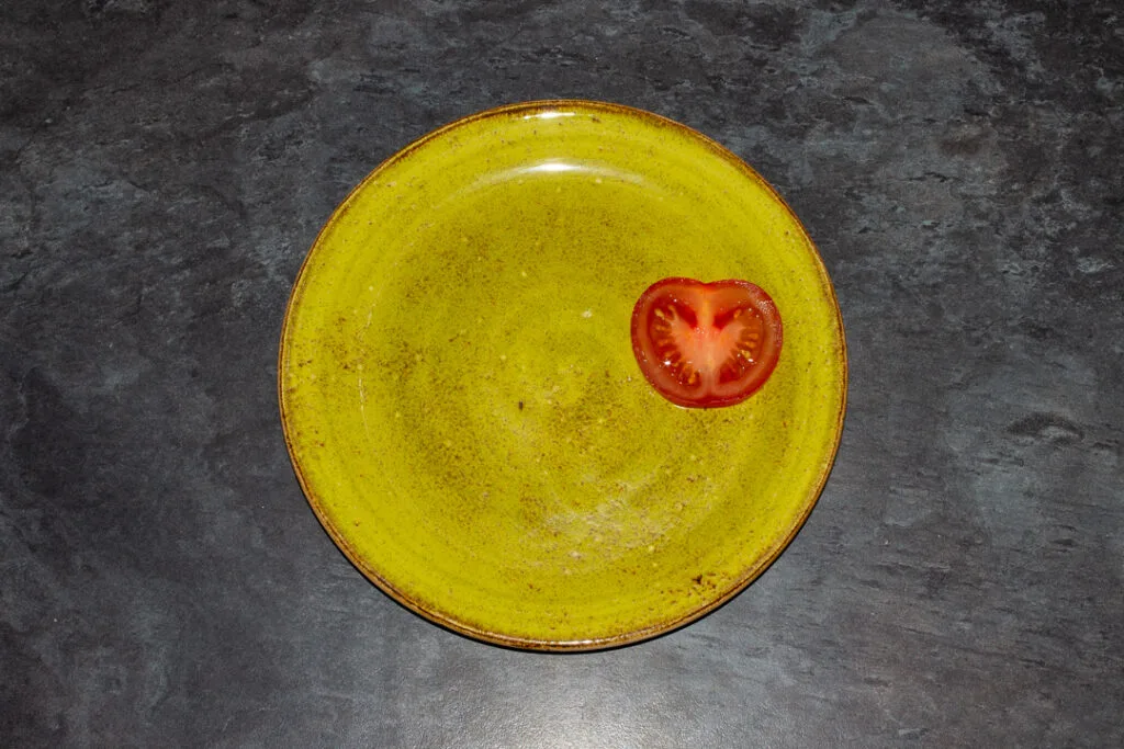 A slice of tomato on a green plate.
