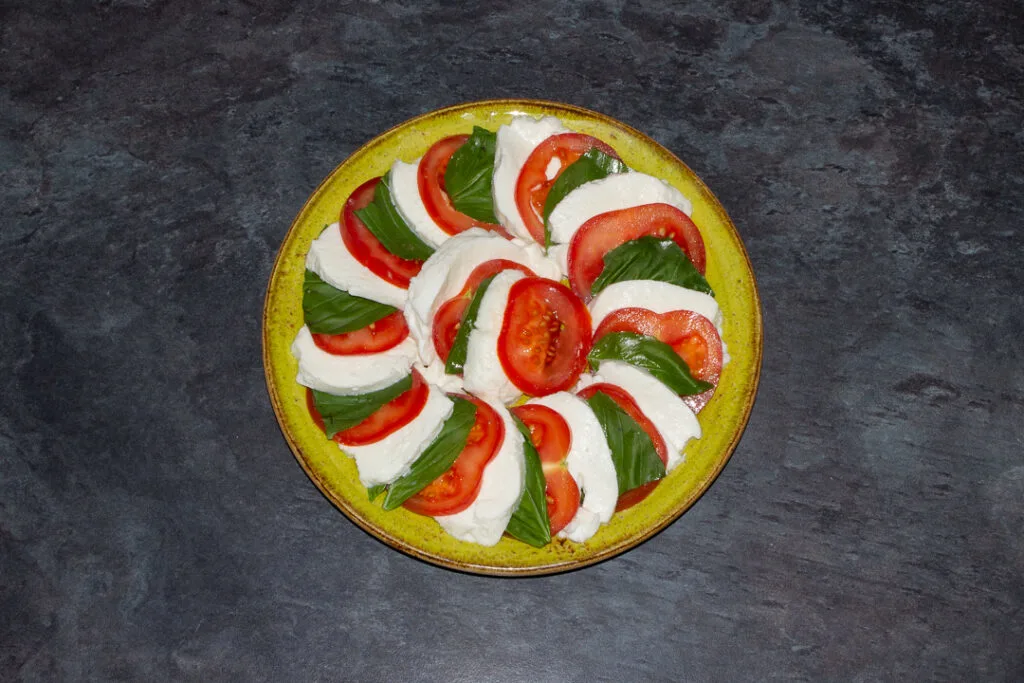 Slices of tomato, basil and mozzarella in a layered circle on a green plate.