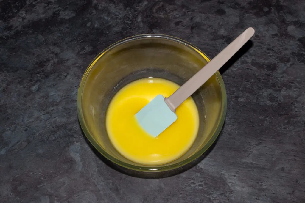 Melted butter in a glass bowl with a rubber spatula in it.